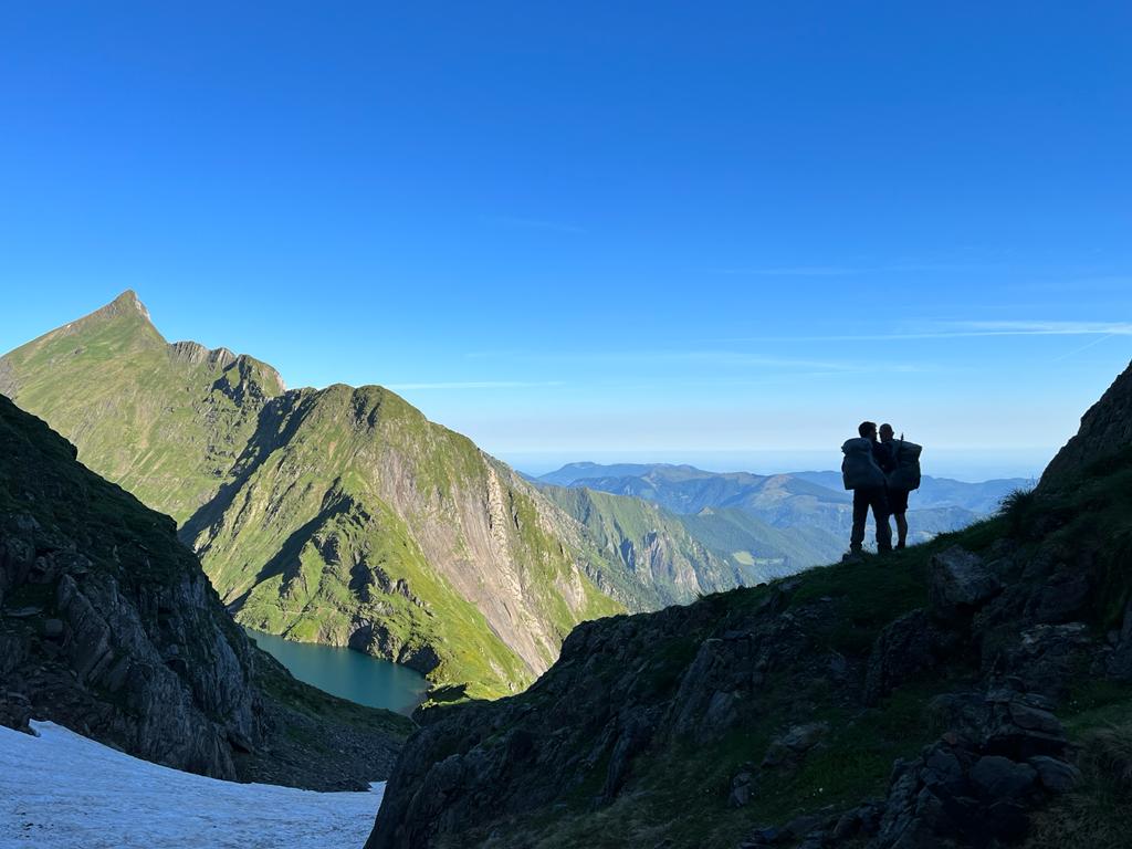 Two figures on a high mountain ridge above an alpine lake at first light
